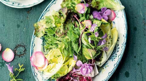Teller mit buntem Salat und Vinaigrette auf einem Holztisch
