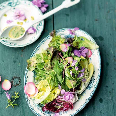 Teller mit buntem Salat und Vinaigrette auf einem Holztisch