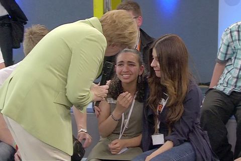 Angela Merkel im grünen Blazer beugt sich zu einem weinenden Mädchen herunter, das ein anderes Mädchen im Arm hält.