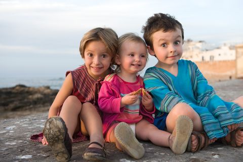 Drei junge Geschwisterkinder sitzen auf einem Hügel