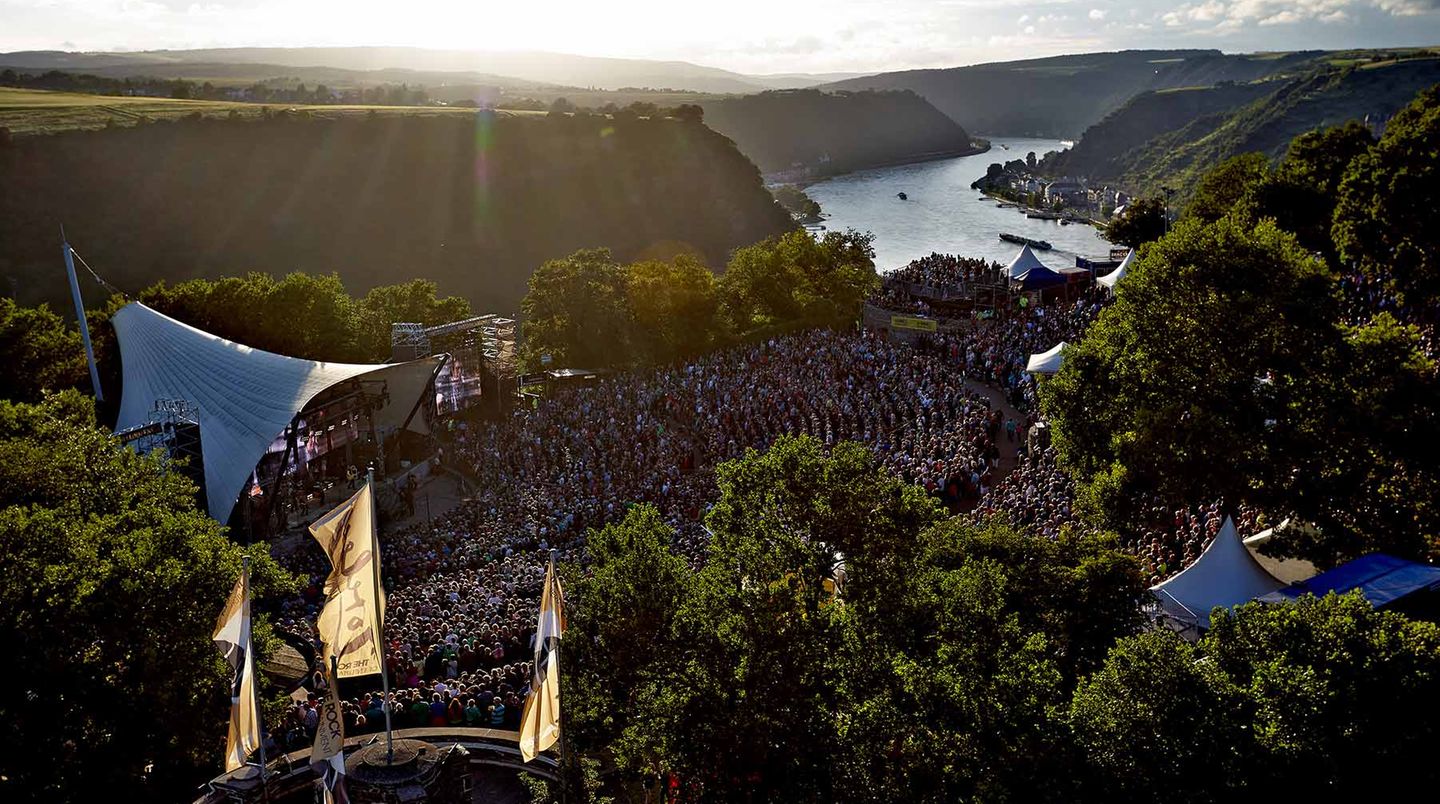 St. Goar - Ein Felsen voller Musik  Zwei deutsche Mythen treffen aufeinander, und beide haben etwas mit Liedern zu tun: die Loreley, jener 132 Meter aufragende Felsen am Rhein, besungen von Heinrich Heine („Ich weiß nicht, was soll es bedeuten“), und der Rockpalast, jene öffentlich-rechtliche Musikshow, die seit Jahrzehnten Konzerte ans Sofa liefert. In den 80er Jahren spielten auf der Freilichtbühne herausragende Künstler wie Joe Cocker, BAP, U2 und Rory Gallagher; heute noch trägt der Ort Spuren dieser Auftritte in sich. Einmal sollte man dabei gewesen sein, wenn „der Gipfel des Berges funkelt im Abendsonnenschein“ (Heine), auch wenn längst nicht mehr alle Bands weltberühmt und aufregend sind.  www.loreley-freilichtbuehne.de  Auf der Lokalpatrioten-Karte anschauen