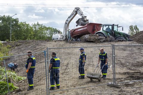 Ein Bagger lädt Schutt in den Anhänger eines Treckers, während im Vordergrund vier Mitarbeiter des THW stehen
