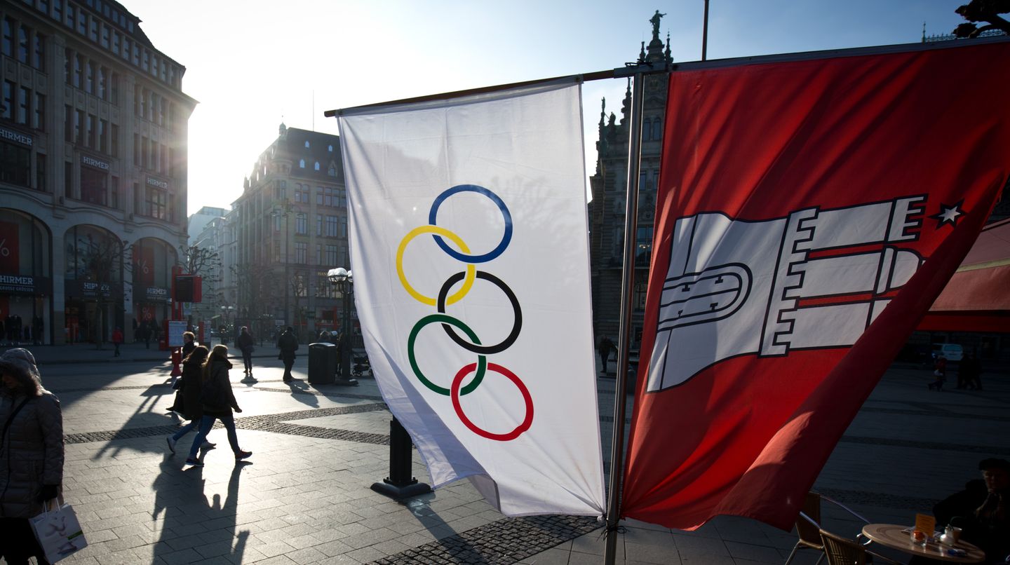 Flaggen mit den Olympischen Ringen und dem Wappen von Hamburg hängen neben einem Straßenkaffee am Rathausmarkt in Hamburg.