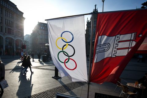 Flaggen mit den Olympischen Ringen und dem Wappen von Hamburg hängen neben einem Straßenkaffee am Rathausmarkt in Hamburg.