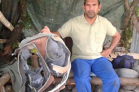 Ein Mitglied eines Strandreinigungsteams hält einen zerschlissenen Koffer in der Hand, der möglicherweise vom vermissten Flug MH370 stammen könnte