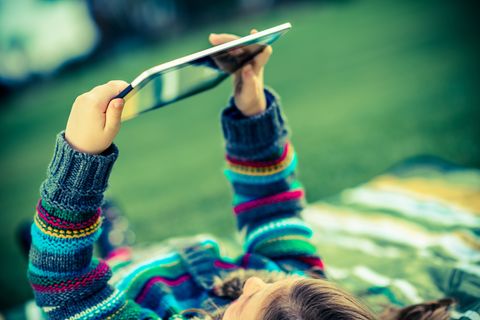Ein Mädchen liegt auf einer Wiese und spielt mit einem Tablet