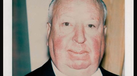 Alfred Hitchcock in Anzug und Krawatte vor unebenem Hintergrund.