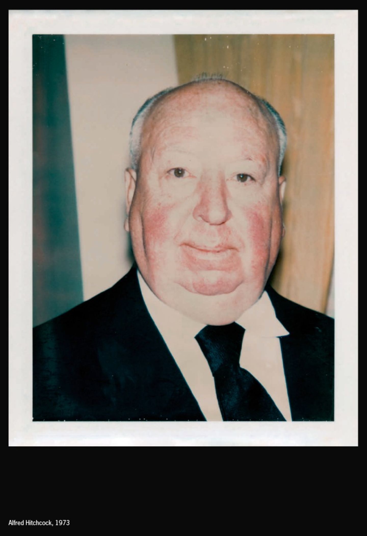 Alfred Hitchcock in Anzug und Krawatte vor unebenem Hintergrund.