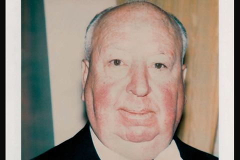Alfred Hitchcock in Anzug und Krawatte vor unebenem Hintergrund.