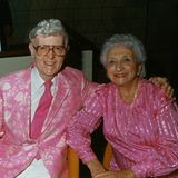 Er in einem rosafarbigen Jacket, sie im farblich passenden Kleid.