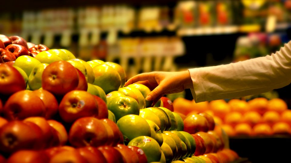 Eine Hand rgeift im Supermarkt zu einem Apfel.