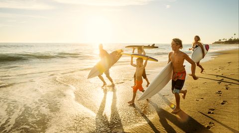 Eine Familie läuft mit Surfbrettern am Strand entlang.