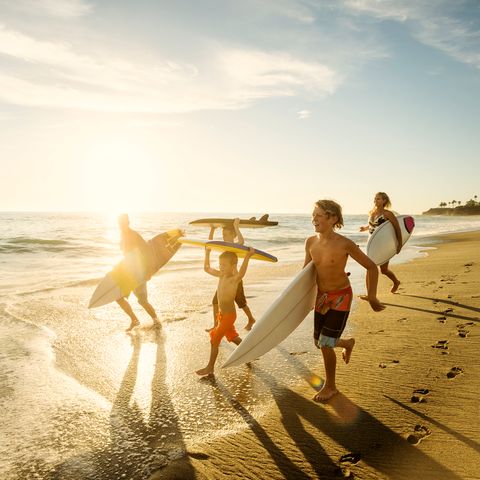 Eine Familie läuft mit Surfbrettern am Strand entlang.