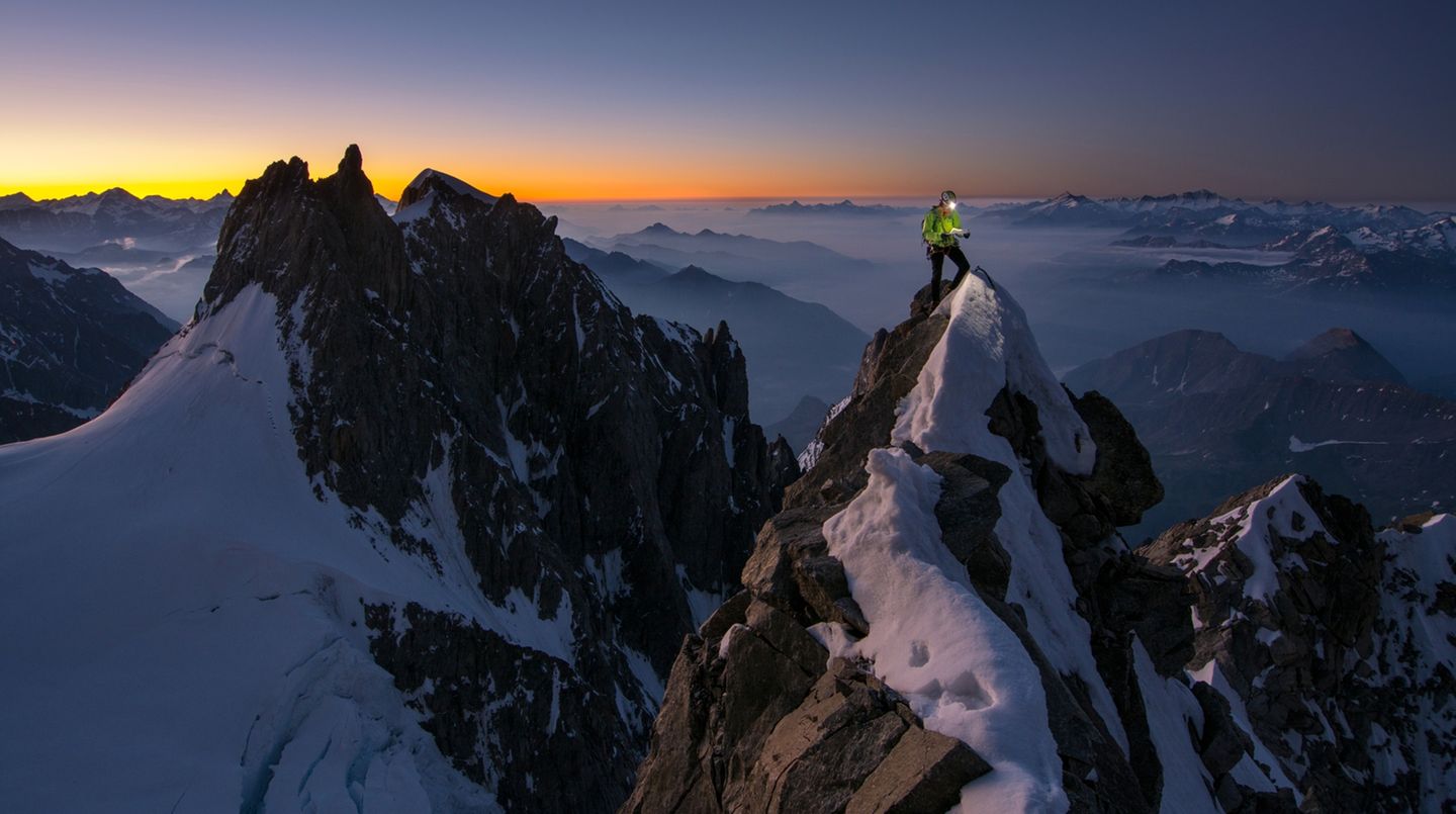 Bergsteiger schaut mit Stirnlampe auf einem Grat in die Routenbeschriebung