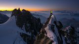 Bergsteiger schaut mit Stirnlampe auf einem Grat in die Routenbeschriebung