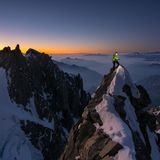 Bergsteiger schaut mit Stirnlampe auf einem Grat in die Routenbeschriebung