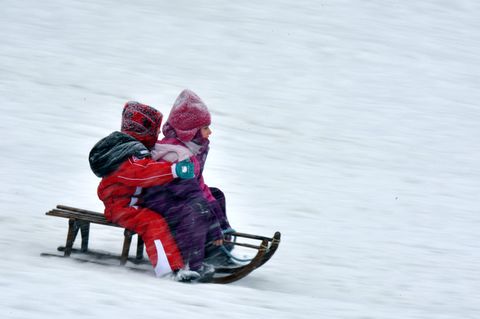 Kinder fahren mit einem Schlitten einen Berg hinab
