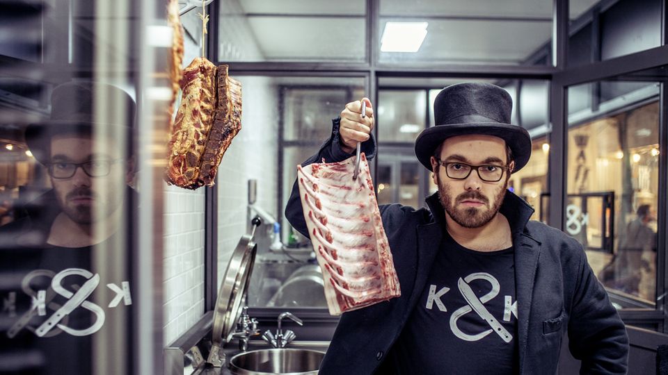 Hendrik Haase steht in seiner Metzgerei "Kumpel & Keule" und hält ein Stück Schweinerippe in die Höhe