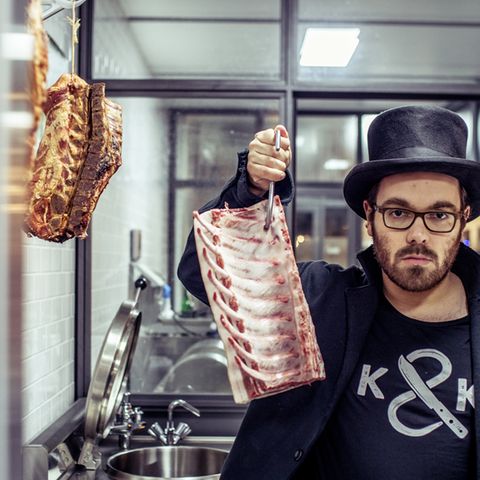 Hendrik Haase steht in seiner Metzgerei "Kumpel & Keule" und hält ein Stück Schweinerippe in die Höhe