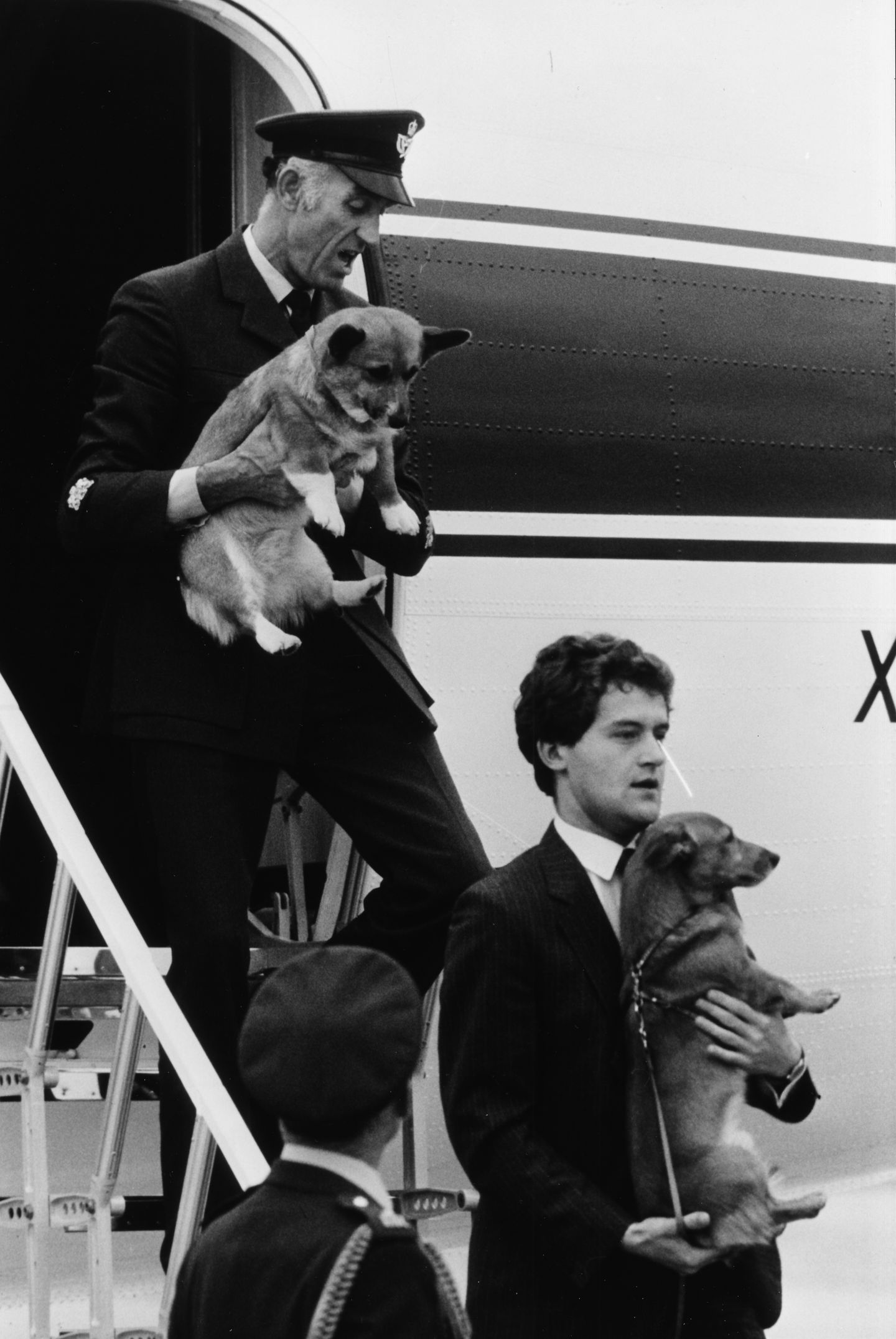 Zwei Diener der Queen tragen zwei Corgis 1983 aus einem Flugzeug
