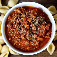 Eine Schale mit Bolognese. Drum herum liegen Nudeln.