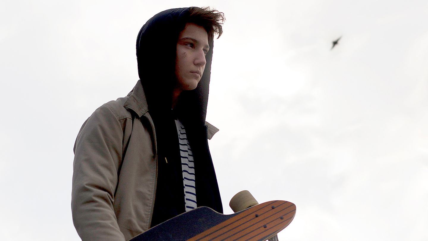 Teenager mit Skateboard unterm Arm schaut ernst