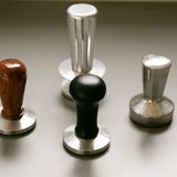 Verschiedene Tamper. Damit bezeichnet man Werkzeuge zum Pressen des gemahlenen Kaffees in einem Siebträger, bevor dieser in die Brühgruppe eingehängt wird. Ein wichtiger Schritt, um das Kaffeemehl gleich hoch und gerade im Sieb zu komprimieren, damit das Wasser einen Widerstand hat und sich gleichmäßig durch den Kaffee bewegen kann und es zu einer guten Extraktion kommt