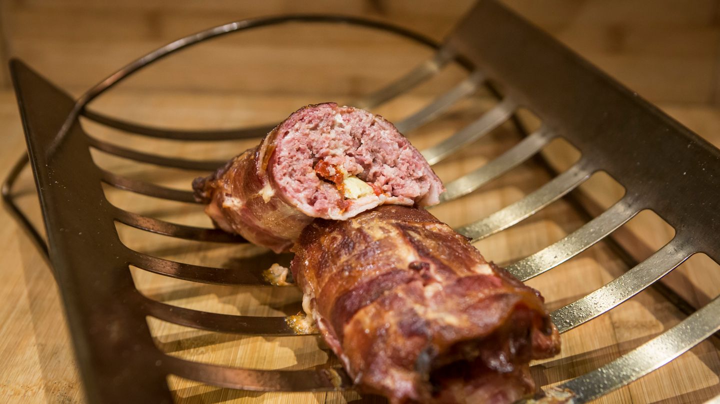 Boston-Bacon-Bomb  In der Welt des BBQ versteht man unter einer Bacon Bomb eine mit Speck umwickelte Hackfleisch- oder Wurstbrätrolle, die geräuchert und dann wie ein Hackbraten in Scheiben geschnitten wird.      Rezept für Boston-Bacon-Bomb mit italienischer Füllung    Für 8 Personen    Zubereitungszeit: 30 Minuten    Grillzeit 1,5-2 Stunden    Zubehör: 1 große handvoll Hickoryholz-Chips, digitales Fleischthermometer        Zutaten:  900 g milde italienische Salsiccia- Würste, Wurstpelle entfernt    30 g Parmesan, fein gerieben    32 dicke Speckscheiben (insgesamt etwa 1¼–1 ½ kg)    60 g eingelegte Artischockenherzen, abgetropft und klein geschnitten    60 g eingelegte getrocknete Tomaten, abgetropft und klein geschnitten    60 g geröstete rote Paprikaschoten (Glas), abgetropft und klein geschnitten        Zubereitung:  1. Die Räucherchips mind. 30 Min. wässern.    2. Den Grill für indirekte schwache Hitze (120–175 °C) vorbereiten.    3. Wurstbrät und Parmesan gründlich, aber behutsam mischen und die Masse in zwei gleich große Portionen teilen.    4. Einen großen Bogen Wachspapier auf die Arbeitsfläche legen und darauf aus 16 Speckscheiben ein Gitter herstellen. Dafür 8 Scheiben waagerecht dicht nebeneinander legen, dann 8 Scheiben senkrecht nebeneinander darüberlegen und die Scheiben miteinander verweben. Das Speckgitter sollte etwa 30 x 30 cm groß sein (gegebenenfalls müssen Sie die Speckscheiben etwas auseinanderziehen).    5. Auf einem zweiten großen Bogen Wachspapier eine der beiden Brätportionen zu einem 20 cm großen, gleichmäßig dicken Quadrat formen. Auf der Brätplatte im Abstand von etwa 5 cm der Ihnen zugewandten Seite die Hälfte der Artischocken, der getrockneten Tomaten und der Paprikaschoten in waagerechten, parallelen Reihen anordnen, dabei an den beiden Enden jeweils 2½ cm zur Brätkante hin frei lassen. Die Brätplatte fest aufrollen und an den Enden zusammendrücken, damit die Füllung gut eingeschlossen ist. Die Bomb sollte jetzt wie ein kleiner Hackbraten aussehen. Die Bomb auf die Ihnen zugewandte Seite des Gitters legen, mithilfe des Wachspapiers das Gitter anheben und die Bomb einwickeln. Mit der Specknaht nach unten beiseitelegen. Aus den übrigen Zutaten eine zweite Bomb herstellen.    6. Die Chips abtropfen lassen, auf die Glut oder in die Räucherbox des Gasgrills geben und den Deckel schließen. Sobald Rauch entsteht, die Bacon Bombs über indirekter schwacher Hitze bei geschlossenem Deckel 1 ½–2 Std. grillen, bis ihre Kerntemperatur an der dicksten Stelle 68 °C beträgt. Vom Grill nehmen und 10 Min. nachziehen lassen (dabei wird sich die Kerntemperatur noch um 2–5 °C erhöhen). In gut 2 cm dicke Scheiben schneiden und servieren.    7. Auf Wachspapier wird das Speckgitter hergestellt. Legen Sie dafür die Scheiben dicht aneinander und verweben Sie sie zu einem etwa 30 x 30 cm großen Gitter.    8. Klein geschnittene Artischocken, Tomaten und Paprika in waagerechten, parallelen Reihen auf der Brätplatte anordnen. Lassen Sie dabei an den Enden etwa 2½ cm zum Rand hin frei.    9. Das Brät aufrollen und die Enden fest zusammendrücken, damit die Füllung gut eingeschlossen ist.    10.  Die Bomb auf das Speckgitter legen und in den Speck wickeln.