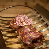 Boston-Bacon-Bomb  In der Welt des BBQ versteht man unter einer Bacon Bomb eine mit Speck umwickelte Hackfleisch- oder Wurstbrätrolle, die geräuchert und dann wie ein Hackbraten in Scheiben geschnitten wird.      Rezept für Boston-Bacon-Bomb mit italienischer Füllung    Für 8 Personen    Zubereitungszeit: 30 Minuten    Grillzeit 1,5-2 Stunden    Zubehör: 1 große handvoll Hickoryholz-Chips, digitales Fleischthermometer        Zutaten:  900 g milde italienische Salsiccia- Würste, Wurstpelle entfernt    30 g Parmesan, fein gerieben    32 dicke Speckscheiben (insgesamt etwa 1¼–1 ½ kg)    60 g eingelegte Artischockenherzen, abgetropft und klein geschnitten    60 g eingelegte getrocknete Tomaten, abgetropft und klein geschnitten    60 g geröstete rote Paprikaschoten (Glas), abgetropft und klein geschnitten        Zubereitung:  1. Die Räucherchips mind. 30 Min. wässern.    2. Den Grill für indirekte schwache Hitze (120–175 °C) vorbereiten.    3. Wurstbrät und Parmesan gründlich, aber behutsam mischen und die Masse in zwei gleich große Portionen teilen.    4. Einen großen Bogen Wachspapier auf die Arbeitsfläche legen und darauf aus 16 Speckscheiben ein Gitter herstellen. Dafür 8 Scheiben waagerecht dicht nebeneinander legen, dann 8 Scheiben senkrecht nebeneinander darüberlegen und die Scheiben miteinander verweben. Das Speckgitter sollte etwa 30 x 30 cm groß sein (gegebenenfalls müssen Sie die Speckscheiben etwas auseinanderziehen).    5. Auf einem zweiten großen Bogen Wachspapier eine der beiden Brätportionen zu einem 20 cm großen, gleichmäßig dicken Quadrat formen. Auf der Brätplatte im Abstand von etwa 5 cm der Ihnen zugewandten Seite die Hälfte der Artischocken, der getrockneten Tomaten und der Paprikaschoten in waagerechten, parallelen Reihen anordnen, dabei an den beiden Enden jeweils 2½ cm zur Brätkante hin frei lassen. Die Brätplatte fest aufrollen und an den Enden zusammendrücken, damit die Füllung gut eingeschlossen ist. Die Bomb sollte jetzt wie ein kleiner Hackbraten aussehen. Die Bomb auf die Ihnen zugewandte Seite des Gitters legen, mithilfe des Wachspapiers das Gitter anheben und die Bomb einwickeln. Mit der Specknaht nach unten beiseitelegen. Aus den übrigen Zutaten eine zweite Bomb herstellen.    6. Die Chips abtropfen lassen, auf die Glut oder in die Räucherbox des Gasgrills geben und den Deckel schließen. Sobald Rauch entsteht, die Bacon Bombs über indirekter schwacher Hitze bei geschlossenem Deckel 1 ½–2 Std. grillen, bis ihre Kerntemperatur an der dicksten Stelle 68 °C beträgt. Vom Grill nehmen und 10 Min. nachziehen lassen (dabei wird sich die Kerntemperatur noch um 2–5 °C erhöhen). In gut 2 cm dicke Scheiben schneiden und servieren.    7. Auf Wachspapier wird das Speckgitter hergestellt. Legen Sie dafür die Scheiben dicht aneinander und verweben Sie sie zu einem etwa 30 x 30 cm großen Gitter.    8. Klein geschnittene Artischocken, Tomaten und Paprika in waagerechten, parallelen Reihen auf der Brätplatte anordnen. Lassen Sie dabei an den Enden etwa 2½ cm zum Rand hin frei.    9. Das Brät aufrollen und die Enden fest zusammendrücken, damit die Füllung gut eingeschlossen ist.    10.  Die Bomb auf das Speckgitter legen und in den Speck wickeln.