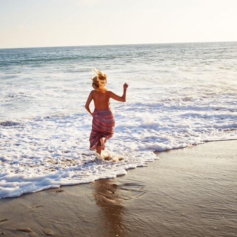 Die Autorin, im Kleid, springt am Strand ins Meer