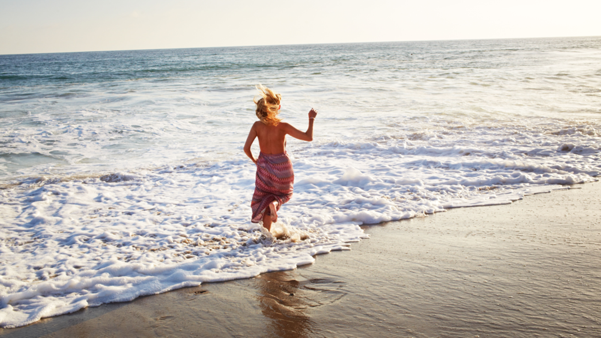 Die Autorin, im Kleid, springt am Strand ins Meer