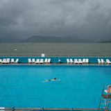 Ein Mann zieht in einem betonierten Schwimmbad seine Bahnen. Direkt dahinter ist das offene Meer zu sehen.