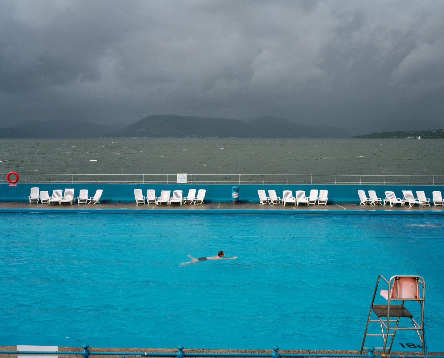 Ein Mann zieht in einem betonierten Schwimmbad seine Bahnen. Direkt dahinter ist das offene Meer zu sehen.