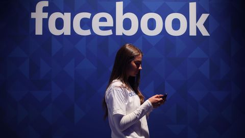 Eine Frau steht mit einem Smartphone vor dem Facebook-Logo