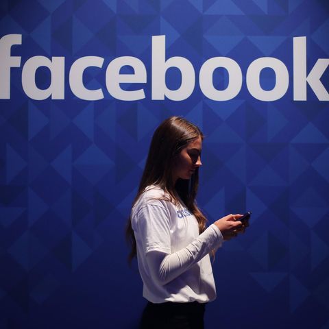 Eine Frau steht mit einem Smartphone vor dem Facebook-Logo