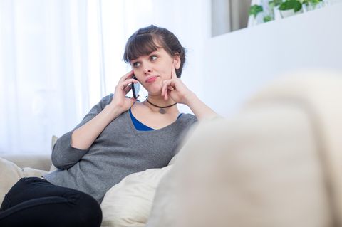 Ein junge Frau sitzt auf dem Sofa und telefoniert. Der EuGH hat die Gebühren für Service-Telefonnummern deckelt.