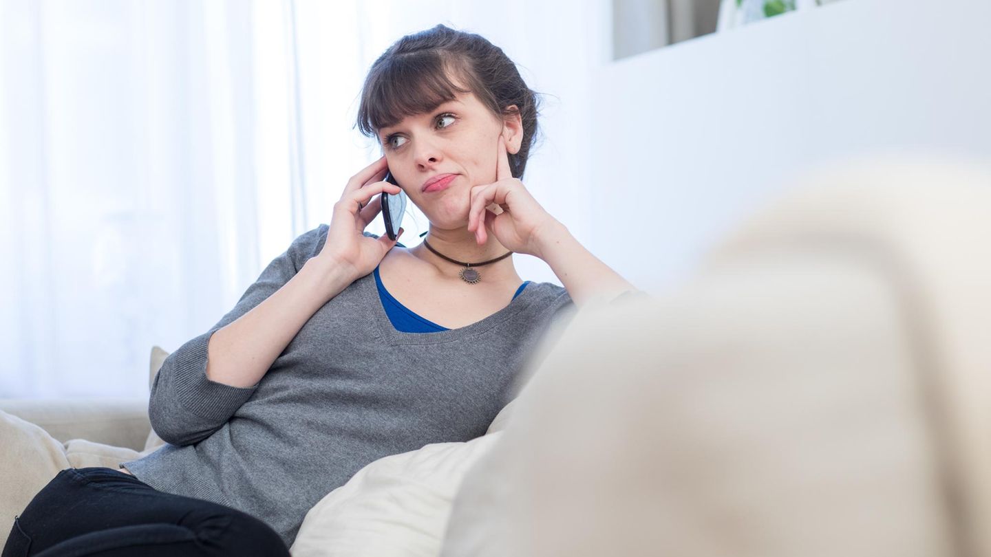 Ein junge Frau sitzt auf dem Sofa und telefoniert. Der EuGH hat die Gebühren für Service-Telefonnummern deckelt.