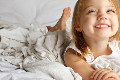 Mädchen liegt im Bett und grinst