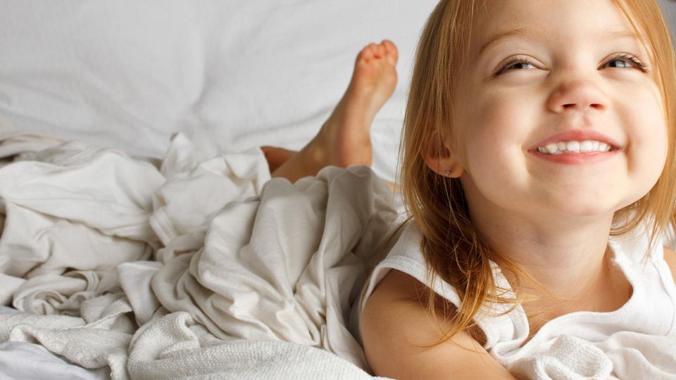 Mädchen liegt im Bett und grinst