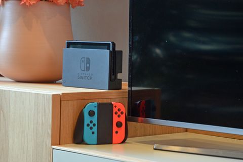 Die Nintendo Switch steht im Dock vor einem Fernseher, daneben die JoyCons in ihrer Halterung
