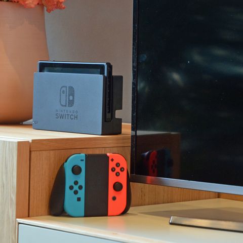 Die Nintendo Switch steht im Dock vor einem Fernseher, daneben die JoyCons in ihrer Halterung