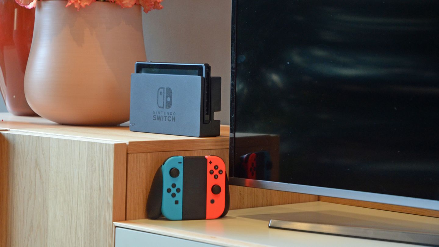 Die Nintendo Switch steht im Dock vor einem Fernseher, daneben die JoyCons in ihrer Halterung