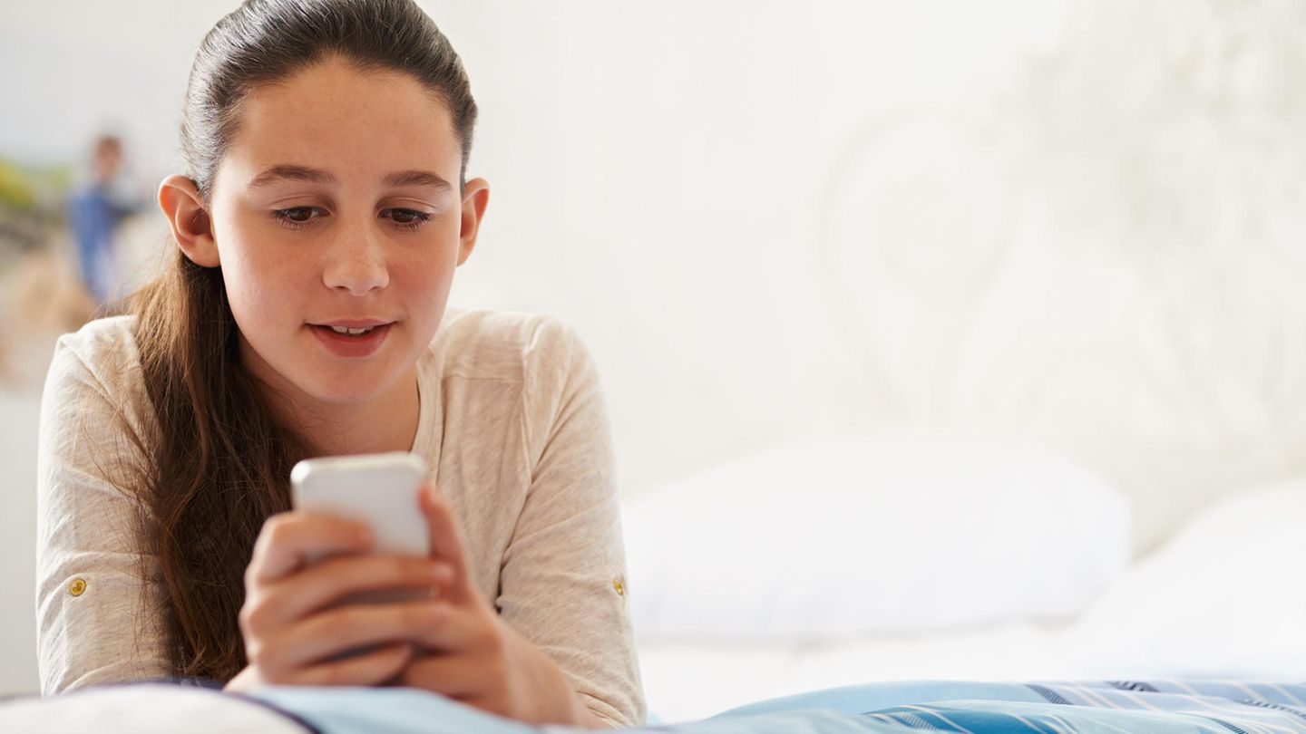 Ein Mädchen liegt mit Handy auf dem Bett
