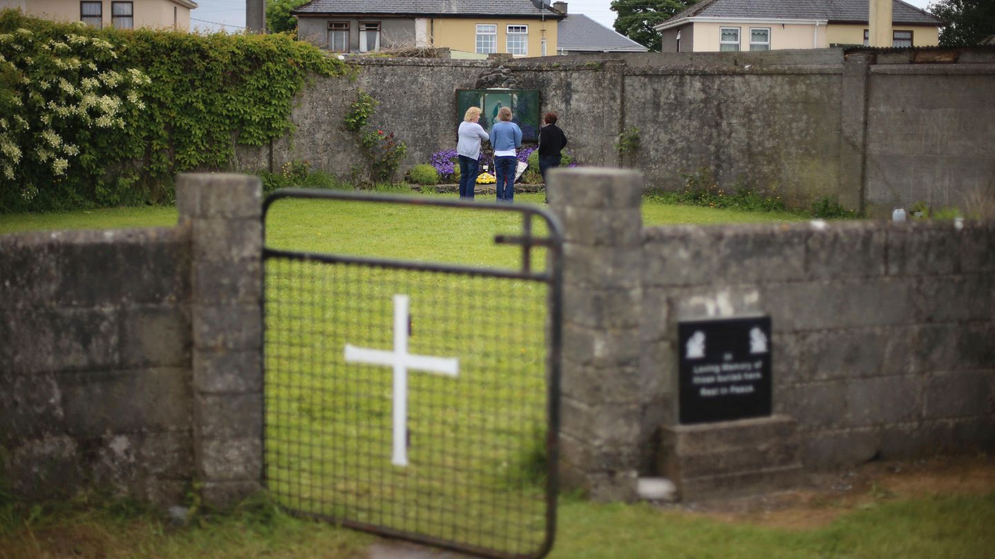 Massengrab für 800 Babys im irischen Tuam: Grüner Rasen, umgeben von einer Mauer mit einem Tor mit weißem Kreuz