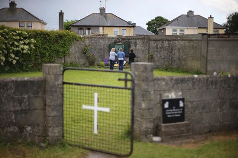 Massengrab für 800 Babys im irischen Tuam: Grüner Rasen, umgeben von einer Mauer mit einem Tor mit weißem Kreuz