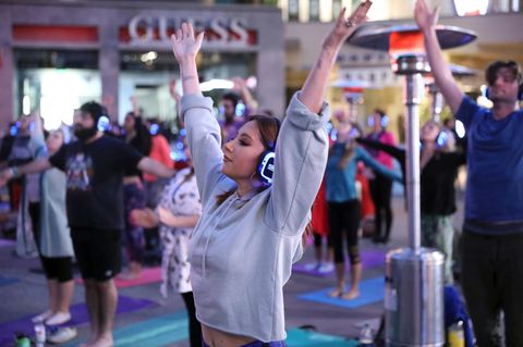 Eine Yogalehrerin vor den Kursteilnehmern. Alle strecken die Arme in die Luft.