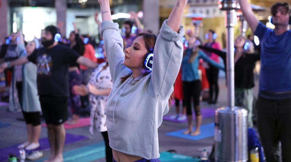 Eine Yogalehrerin vor den Kursteilnehmern. Alle strecken die Arme in die Luft.