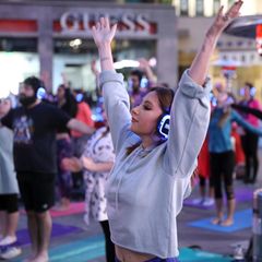 Eine Yogalehrerin vor den Kursteilnehmern. Alle strecken die Arme in die Luft.