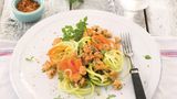 Gemüsespaghetti mit Hähnchen-Bolognese  Zutaten:  400 g Hähnchenbrust, 1 Zwiebel, 1 Knoblauchzehe, 2 EL Olivenöl, 2 EL Tomatenmark, 100 ml Gemüsebrühe, 50 g süße Sahne, Meersalz, frisch gemahlener schwarzer Pfeffer, 3 Stängel Oregano, 2 Karotten, 1 Kohlrabi, 2 dünne Zucchini, 1 Bund Petersilie, Saft von ½ Zitrone, Chilisalz (alternativ Cayennepfeffer und Salz), 2 Stängel Basilikum      Zubereitung:  1. Für die Bolognese die Hähnchenbrust grob würfeln und durch die grobe Scheibe des Fleischwolfs lassen. Zwiebel und Knoblauch abziehen und würfeln. 1 EL Olivenöl in einem Bräter erhitzen, das Fleisch darin kurz scharf anbraten. Die Zwiebel- und Knoblauchwürfel zugeben und anschwitzen. Das Tomatenmark unter Rühren anrösten. Mit Gemüsebrühe und Sahne aufgießen, Salz und Pfeffer zugeben. Den Oregano abbrausen, trocken schütteln und zugeben. Die Sauce bei mittlerer Temperatur offen 15 Minuten köcheln lassen.        2. Inzwischen das Gemüse waschen, die Karotten und den Kohlrabi schälen.  Mit Hilfe eines Spiralschneiders das Gemüse in lange dünne Spaghetti schneiden. Die Petersilie abbrausen, trocken schütteln und hacken.        3. Das restliche Olivenöl in einer Pfanne erhitzen, die Gemüsespaghet ti darin etwa 2 Minuten anschwitzen. Mit Salz und Pfeffer bestreuen. Oregano aus der Sauce nehmen und die Sauce mit Zitronensaft und Chilisalz abschmecken, die Petersilie unterrühren.        4. Die Gemüsespaghetti mit der Sauce anrichten. Basilikum waschen, trocken schütteln und die Blätter darüber streuen.