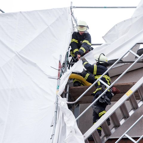 Feuerwehrleute sichern in Hamburg an einem Mehrfamilienhaus Planen an einem Gerüst, die sich durch starken Sturm gelöst haben